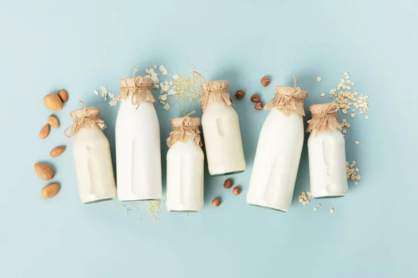 Vegan non dairy plant based milk in bottles and ingredients on turquoise background almond, hazelnut, rice, oat, soy . Alternative lactose free milk substitute. Top view