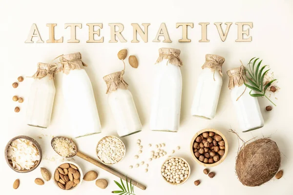 Vegan non dairy plant based milk in bottles and ingredients on light background almond, hazelnut, rice, oat, soy with alternative lettering. Alternative lactose free milk substitute. Top view