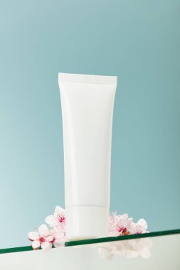 Unbranded white squeeze bottle cosmetic tube on glass transparent shelf, blue background. SPA natural organic beauty product packaging design, branding. Beauty salon mockup, low angle view, below the