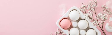Paskalya konsepti. Beyaz seramik tutucuda yumurtalar ve pembe arka planda çiçekler, düz konum, kopyalama alanı