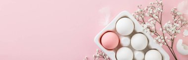 Paskalya konsepti. Beyaz seramik tutucuda yumurtalar ve pembe arka planda çiçekler, düz konum, kopyalama alanı