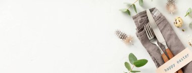 Easter table decorations. Stylish Easter brunch table setting with vintage cutlery, easter eggs and spring branches on light grey background top view flat lay copy space