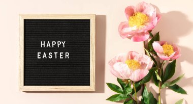Taze bahar çiçekleriyle çevrili Mutlu Paskalyalar yazan bir mektup tahtası.
