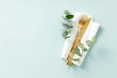 Gold Cutlery with eucalyptus branches on white linen napkin over blue Background. Minimalistic design. Copy Space