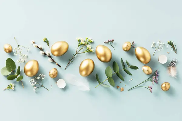 Osterkomposition Aus Goldenen Wachteleiern Federn Und Frühlingsblumen Vor Pastellblauem Hintergrund Stockfoto