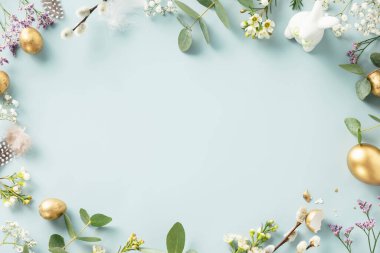 Paskalya masa süslemeleri. Altın Paskalya yumurtaları, tüyler ve mavi arka planda bahar çiçekleri olan Paskalya konseptiniz kutlu olsun. Düz konum görünümü kopyalama alanı çerçeve kenarı