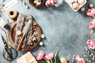 Easter table setting with spring flowers and cutlery on dark blue background top view flat lay. Happy Easter holiday concept for cafes and restaurants. Copy space
