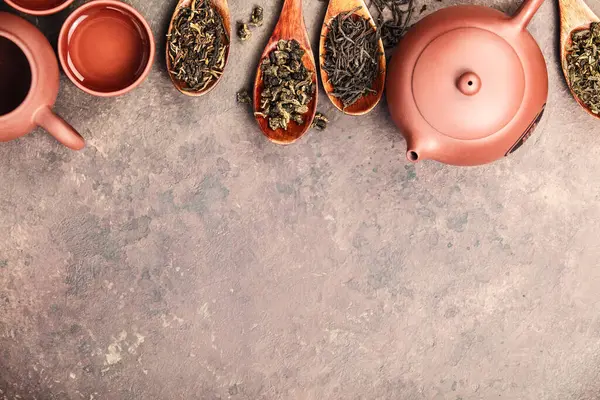 木製のスプーンに飾られたゆったりとした茶葉の品揃え 石の背景に伝統的な陶磁器ティーポットとカップ ストック画像