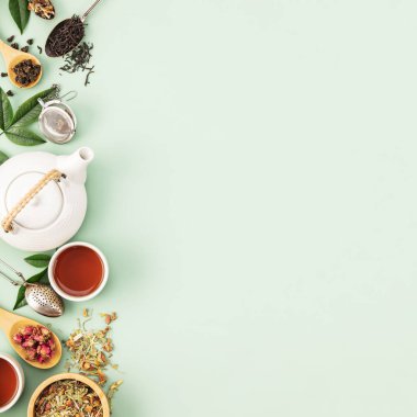 Yumuşak pastel yeşil arka planda çeşitli yaprak çayları, beyaz çaydanlık ve çay aksesuarları içeren iyi düzenlenmiş bir daire, sakin bir çay hazırlama sahnesini betimliyor..