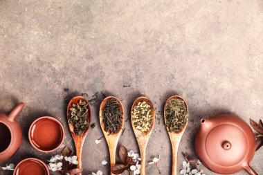 Tahta kaşıklarda seramik çaydanlık ve taştan arka planda fincanlarla sergilenen gevşek çay yaprakları.