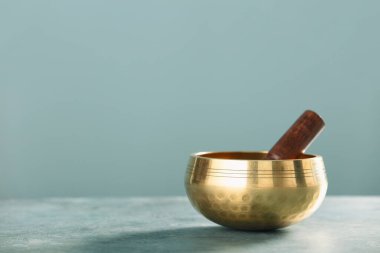 Masanın üzerine tahta bir tokmak yerleştirilmiş altın Tibet şarkı kasesi meditasyon çalışmalarında huzuru ve farkındalığı simgeliyor..