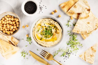 Üzerinde nohut, siyah susam tohumu ve mikroyeşillik bulunan zeytinyağı serpilmiş bir kase pürüzsüz humus mermer zemin üzerinde pita ekmeği ile servis edilir. Sağlıklı bir Akdeniz atıştırması..