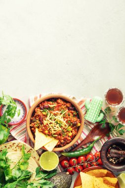 Peynirle kaplanmış Meksika usulü acılı kırmızı biberli karne manzarası. Etrafı nacho, tortilla, sebze ve otlarla çevrili..