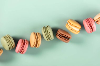 Nane yeşili arka planda çapraz dizilmiş çeşitli renkte Fransız kurabiyeleri. Asgari, canlı ve tatlı temalı.