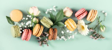 Yumuşak bir nane yeşili yüzeyde gül ve kır çiçekleriyle sıralanmış renkli badem kurabiyeleri. Tatlı, çiçekli ve bahar esintili estetik..