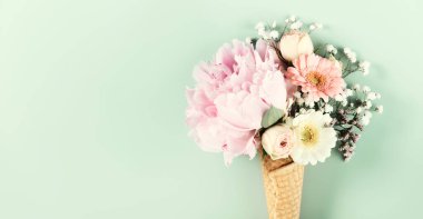 Nane yeşili arka planda dondurma külahında şekillendirilmiş yaratıcı pastel çiçekleri. Kaprisli ve taze çiçek tasarımı.