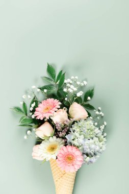 Yumuşak yeşil arka planda dondurma külahında düzenlenmiş pastel çiçeklerden oluşan yaratıcı buket kapris ve zarafeti birleştirir..