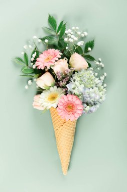 Yumuşak yeşil arka planda dondurma külahında düzenlenmiş pastel çiçeklerden oluşan yaratıcı buket kapris ve zarafeti birleştirir..