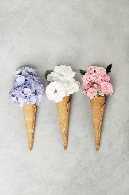 Gri desenli bir yüzeye dizilmiş ortanca, beyaz güller ve pembe karanfillerle dolu yaratıcı waffle konileri..