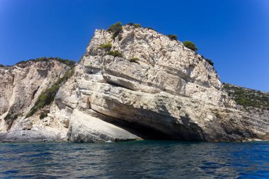 Yükselen kireçtaşı kayalıkları güneşli bir gökyüzünün altında mavi denizle buluşuyor, doğanın muhteşem manzarasını ve gücünü sergiliyor..
