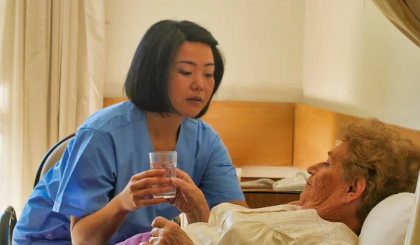 年轻的亚洲女医生帮助在医院病床上吃药的老年退休妇女 — 图库照片