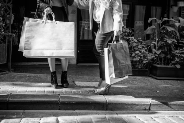 两个漂亮的姑娘沿着城市街道购物 她们穿着细长的腿和购物袋 — 图库照片