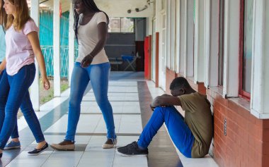 Genç çocuk okulda üzgün bir şekilde yalnız oturuyor. Depresyondaki Afrikalı çocuk koridorda terk edilmiş ve tuğla duvara yaslanmış. Zorbalık, ayrımcılık ve ırkçılık kavramı.