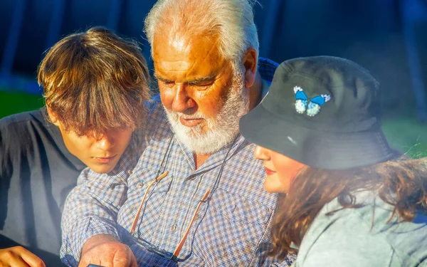 Дедушка Просматривает Снимки Компактной Камеры Открытом Воздухе Своими Внуками — стоковое фото