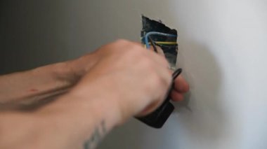 Elektrikçiyim. Evin duvarına elektrik prizi kuran adama yaklaş. Erkek elektrikçi cıvataları sıkmak için tornavida kullanıyor.