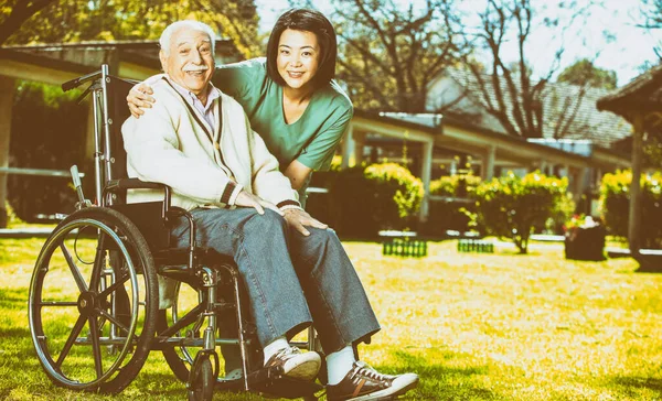 Caucasian senior on the wheelchair smiling with nurse outdoor. Retired elderly people living their life at its best