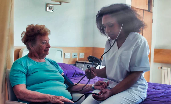 African female doctor visiting elderly female patient in hospital bed. Rehabilitation and retirement concept.