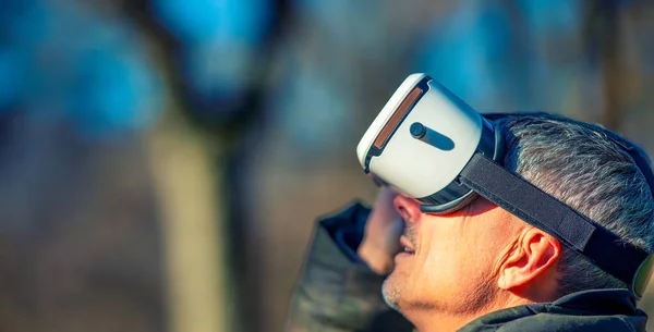 Happy man wearing a virtual reality visor exploring the city park.