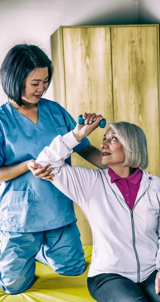 Elder woman making exercises at hospital gym with nurse help.