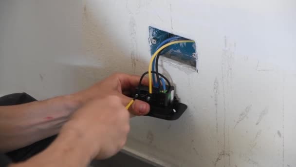 電気工がやってる 家の部屋の壁にコンセントを設置する男のクローズアップ 男性電気技師はボルトを締め付けるためにドライバを使用します — ストック動画
