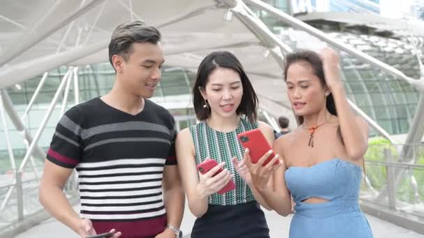 三个亚洲朋友在城市里散步 看着智能手机 幸福与旅游概念 — 图库视频影像