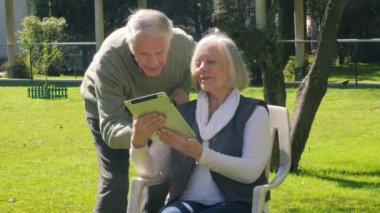 Active seniors concept. Elderly couple in teh garden using tablet.