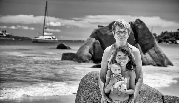 Young girl embracing grand mother on a beautiful tropical beach of Seychelles, holiday and travel concept.