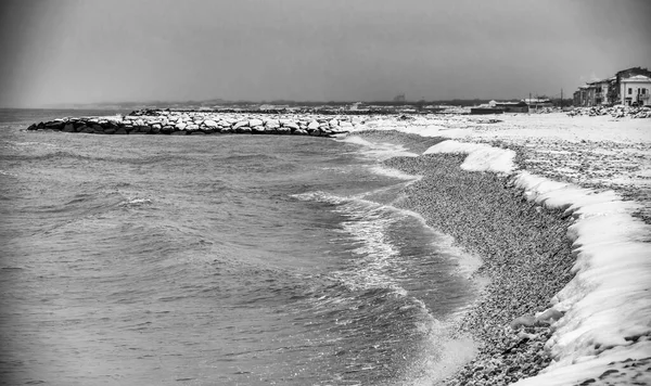 Rocks above the sea covered in snow after a snowstorm. Weather and climate change concept.