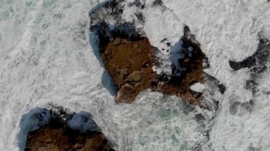 Powerful waves against ocean rocks, overhead super slow motion aerial view on a stormy and sunny day.