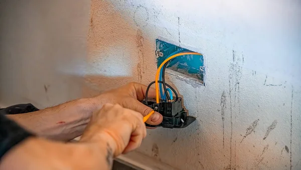 Electrician mounts an electrical outlet to the wall, connecting cables.