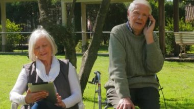 Active seniors. Elderly couple in the garden using smartphone and tablet