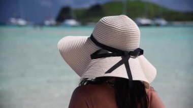 Back view of beautiful woman wearing straw hat looking at the sea on a beautiful tropical beach, slow motion.