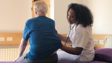 A nurse helps an elderly man on hospital bed.