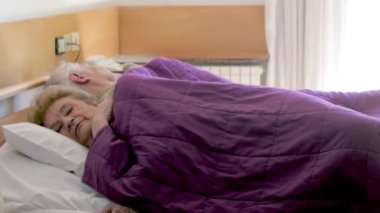 An elderly couple sleeping in hospital bed.