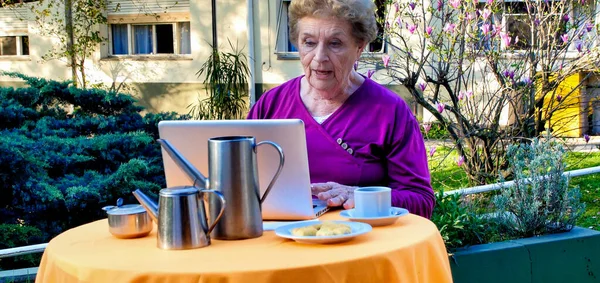 コーカサスの退職した女性は ビデオコールを持って 朝食のために庭でリラックスしたラップトップを使用しています 技術とリラクゼーションの概念 — ストック写真