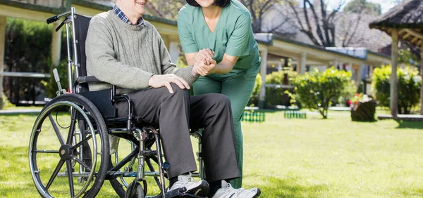 Asian nurse happy with caucasian elder patient on wheelchair, outdoor view.