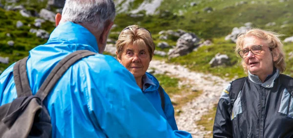 Elderly people relaxing at the end of a mountain hike, talking along the alpin trail