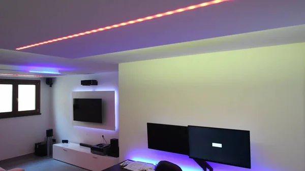 Led strips lighting in a modern living room with sofa, desk and TV screen.