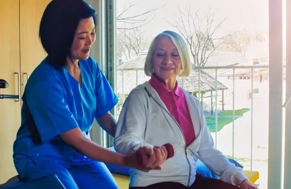 リハビリテーションの概念 高齢者引退女性のトレーニング腕のジムで専門家アジアの女性トレーナーによって監督 — ストック写真