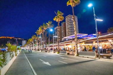 Malaga, İspanya - 14 Nisan 2023: Turistler gece liman boyunca yürüyorlar.